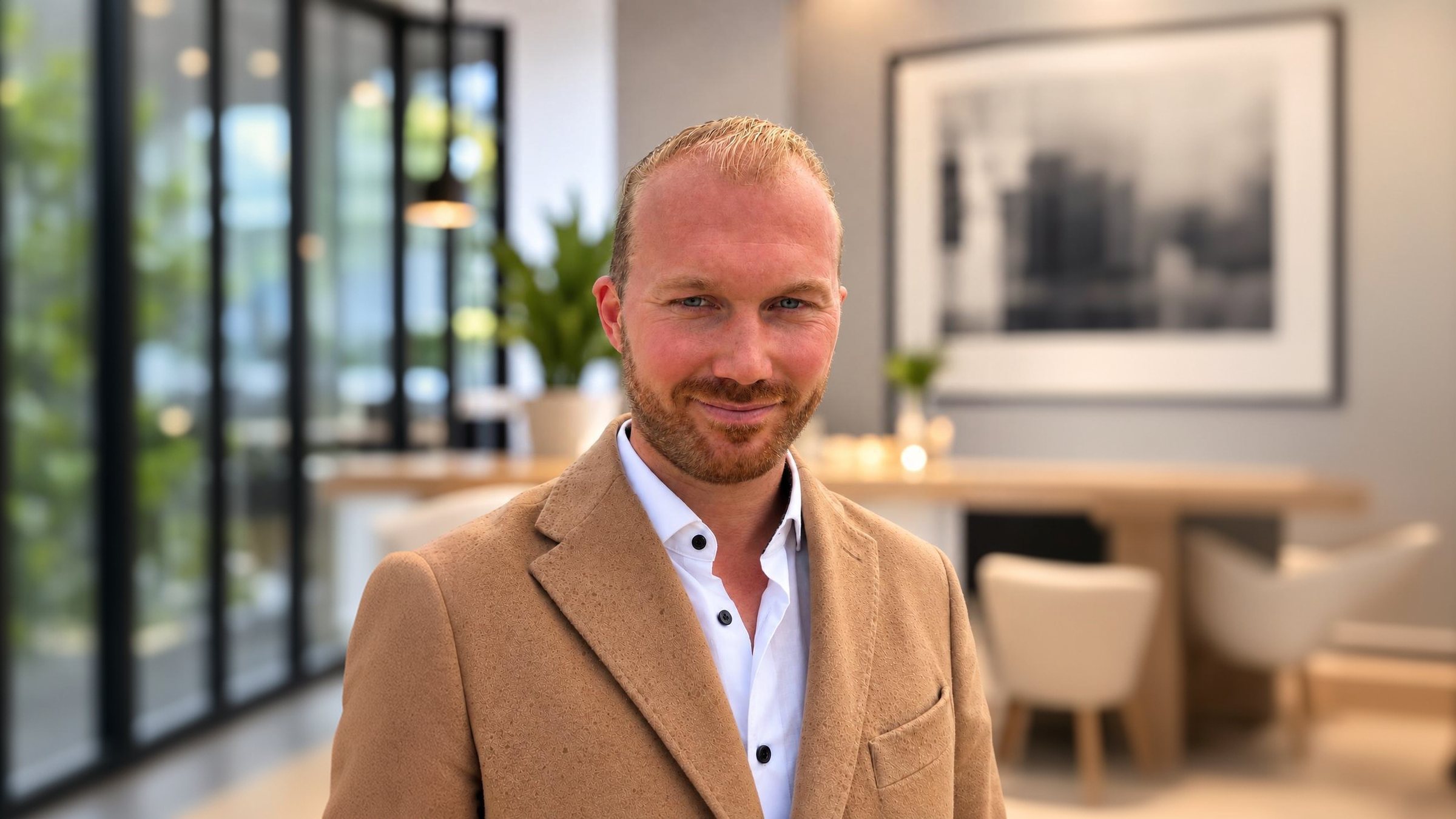 Michael Hoppe im camelfarbenen Mantel und weißen Hemd vor hellem Interieur