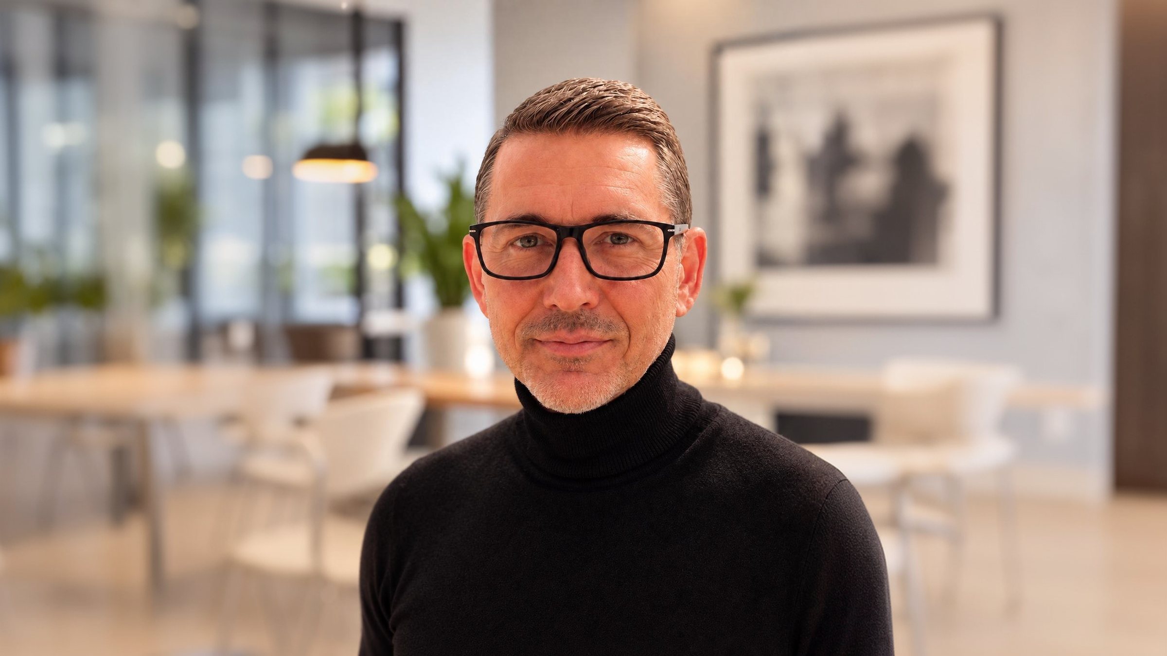 Michael Gleissner mit Brille im schwarzen Rollkragenpullover vor hellem Interieur